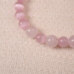 Close-up of rose quartz bracelet showing polished pink beads and shiny bow charm details.