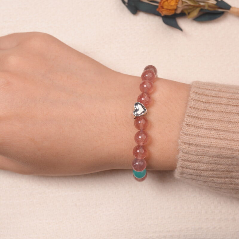 A model wearing the Strawberry Quartz and Angelite bracelet on their wrist. The heart-shaped silver charm adds a touch of elegance and the combination of soothing stones promotes calm and balance.