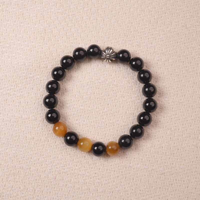 A close-up of the Obsidian and Tiger Eye bracelet, featuring black Obsidian beads paired with golden Tiger Eye stones, finished with a silver flower charm.