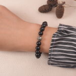 A hand wearing the Obsidian and Tiger Eye bracelet, showing the harmonious mix of black and gold stones with a silver flower accent.