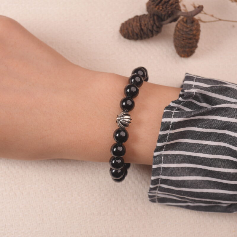 A hand wearing the Obsidian and Tiger Eye bracelet, showing the harmonious mix of black and gold stones with a silver flower accent.