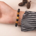 A hand wearing the Obsidian and Tiger Eye bracelet, showing the harmonious mix of black and gold stones with a silver flower accent.
