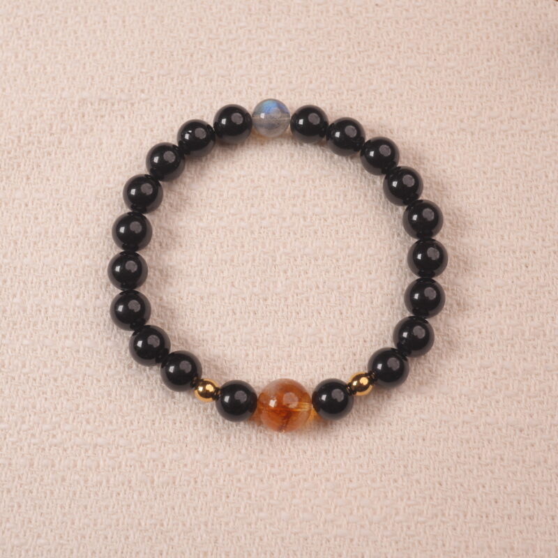 A close-up of an Obsidian, Citrine, and Moonstone bracelet. The dark black Obsidian beads, golden Citrine beads, and iridescent Moonstone bead create a stunning contrast and a powerful energy combination.