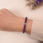 A hand wearing the Amethyst and Aquamarine bracelet. The purple and light blue gemstones create a soothing and elegant accessory for the wrist.