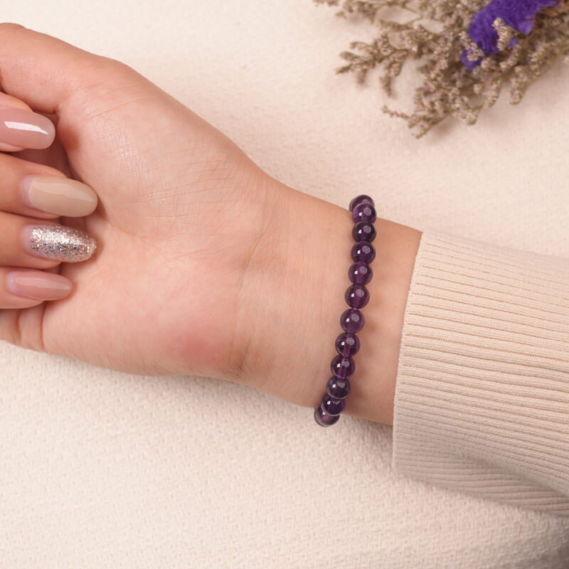 A hand wearing the Amethyst and Aquamarine bracelet. The purple and light blue gemstones create a soothing and elegant accessory for the wrist.