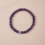 A close-up of an Amethyst and Aquamarine bracelet, featuring polished purple Amethyst beads and a single pale blue Aquamarine bead. The combination of rich purple and light blue creates a calming and balanced look.