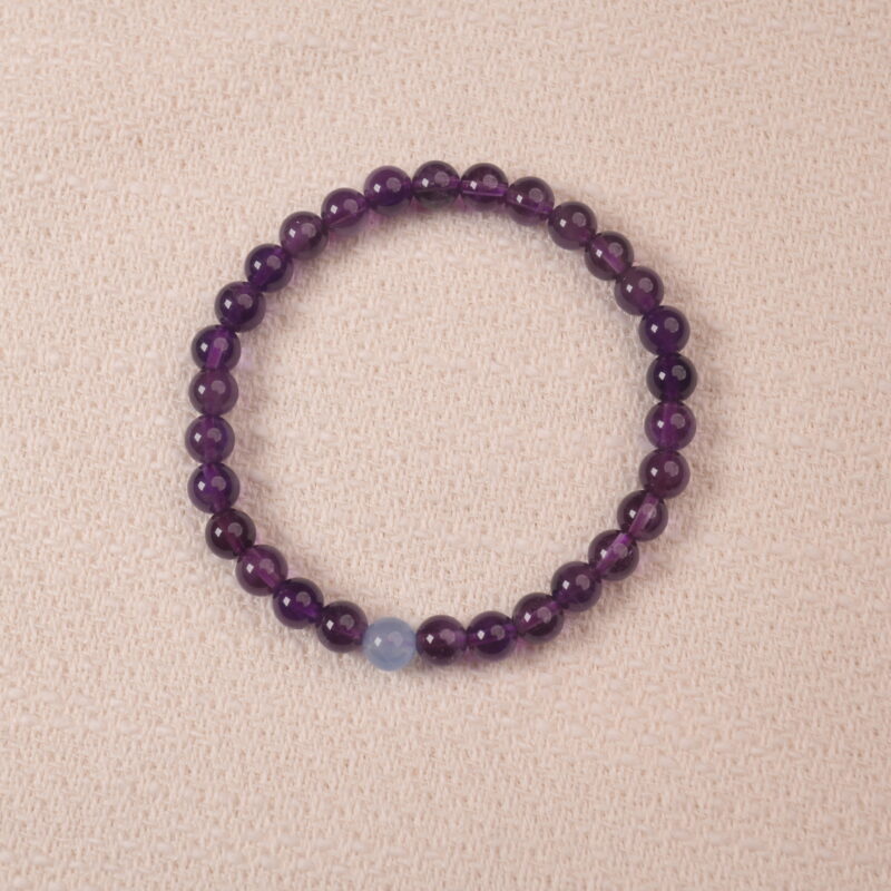 A close-up of an Amethyst and Aquamarine bracelet, featuring polished purple Amethyst beads and a single pale blue Aquamarine bead. The combination of rich purple and light blue creates a calming and balanced look.