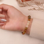 A hand wearing the Yellow Chalcedony and White Chalcedony bracelet, showcasing the warm golden and soft white beads with a silver spacer. The bracelet adds a sophisticated touch to the wrist, making it a versatile accessory for various occasions.