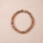 A close-up of a Peach Moonstone bracelet, featuring smooth, polished beads in warm orange tones. The bracelet is accented with silver spacer beads, creating a harmonious contrast between the gemstones.