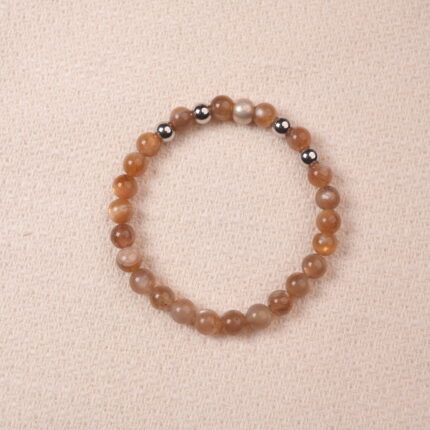 A close-up of a Peach Moonstone bracelet, featuring smooth, polished beads in warm orange tones. The bracelet is accented with silver spacer beads, creating a harmonious contrast between the gemstones.