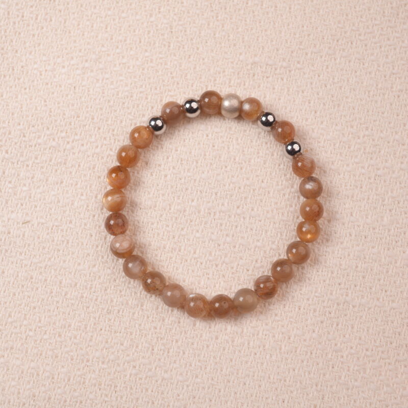 A close-up of a Peach Moonstone bracelet, featuring smooth, polished beads in warm orange tones. The bracelet is accented with silver spacer beads, creating a harmonious contrast between the gemstones.