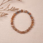 The Peach Moonstone bracelet placed on a soft fabric background, surrounded by delicate natural elements. The combination of warm orange gemstones creates a peaceful and serene ambiance.