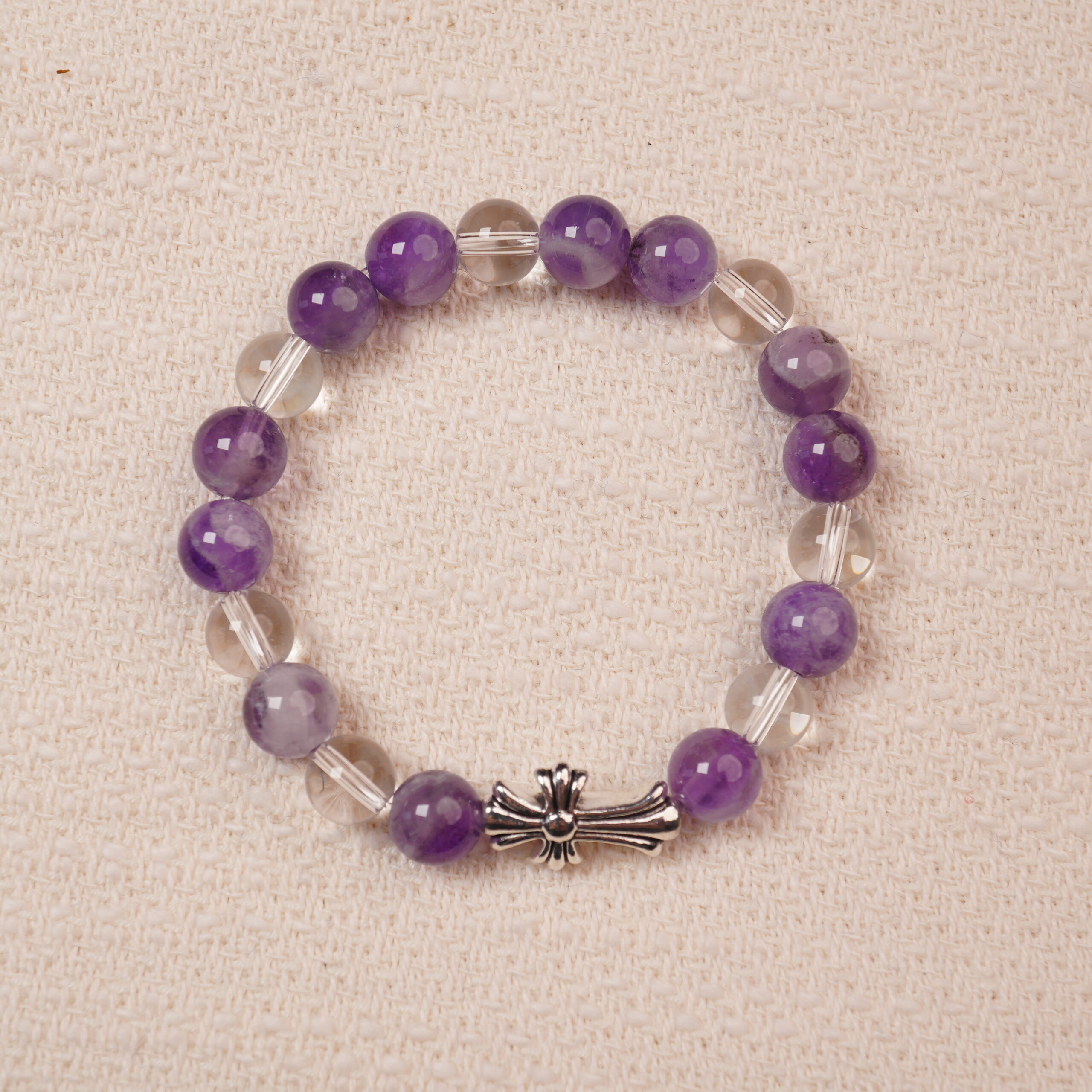 amethyst-clear-quartz-bracelet-main A beautiful bracelet featuring Amethyst and Clear Quartz beads, with a stylish silver cross accent. The smooth, vibrant purple amethyst is complemented by the transparent, calming clear quartz, making this piece perfect for adding balance and tranquility to your collection.