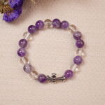 The Amethyst and Clear Quartz bracelet laid on a soft fabric background, highlighting the vibrant colors of the amethyst and the clear beauty of the quartz. The silver cross charm adds an elegant touch.