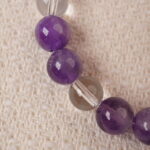 Close-up of the Amethyst and Clear Quartz bracelet showing the smooth texture of the beads and the intricate silver cross accent. The vibrant purple of the amethyst stands out beautifully against the transparent clear quartz.