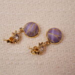 Close-up of the purple embroidered earrings with intricate gold detailing and a sparkling stone, offering a sophisticated and elegant design.