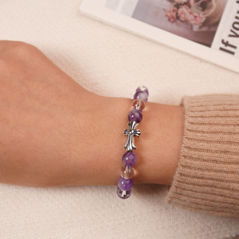 A model wearing the Amethyst and Clear Quartz bracelet on their wrist, showing the front view. The vibrant purple of the amethyst and the transparent clear quartz are beautifully displayed with the silver cross charm at the center.