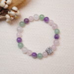 Flat lay of a rose quartz, amethyst, and green aventurine bracelet with a silver rose charm.