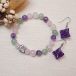 The Rose Quartz, Amethyst, and Green Aventurine bracelet set with Amethyst Merkaba earrings placed next to delicate flowers, showcasing their elegant design and the calming energy they bring.