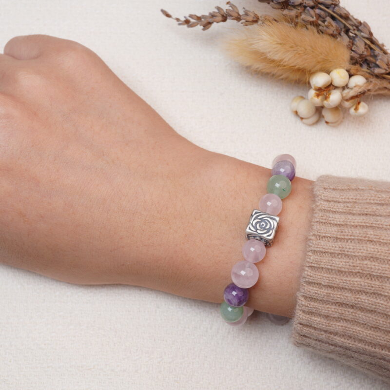 A wrist wearing a bracelet featuring rose quartz, amethyst, green aventurine, and a silver rose charm.