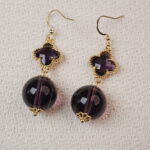 Close-up of the Amethyst earrings, featuring large round Amethyst stones with a sleek, golden setting, offering a sophisticated look with a touch of sparkle.
