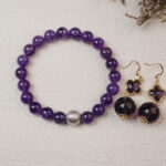 The Amethyst bracelet and earrings placed together on a soft fabric background, accented with delicate flowers, creating a serene and luxurious aesthetic.