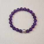 Amethyst beaded bracelet with a textured silver center bead displayed on a soft fabric background.