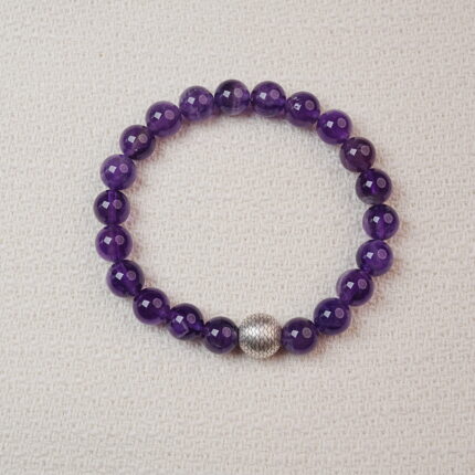 Amethyst beaded bracelet with a textured silver center bead displayed on a soft fabric background.