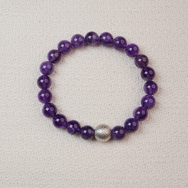 Amethyst beaded bracelet with a textured silver center bead displayed on a soft fabric background.
