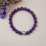 Amethyst bracelet with a silver bead placed beside dried flowers on a soft background.