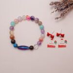 A styled scene featuring multicolor gemstone bracelet with gold accents and Santa earrings with a festive look.