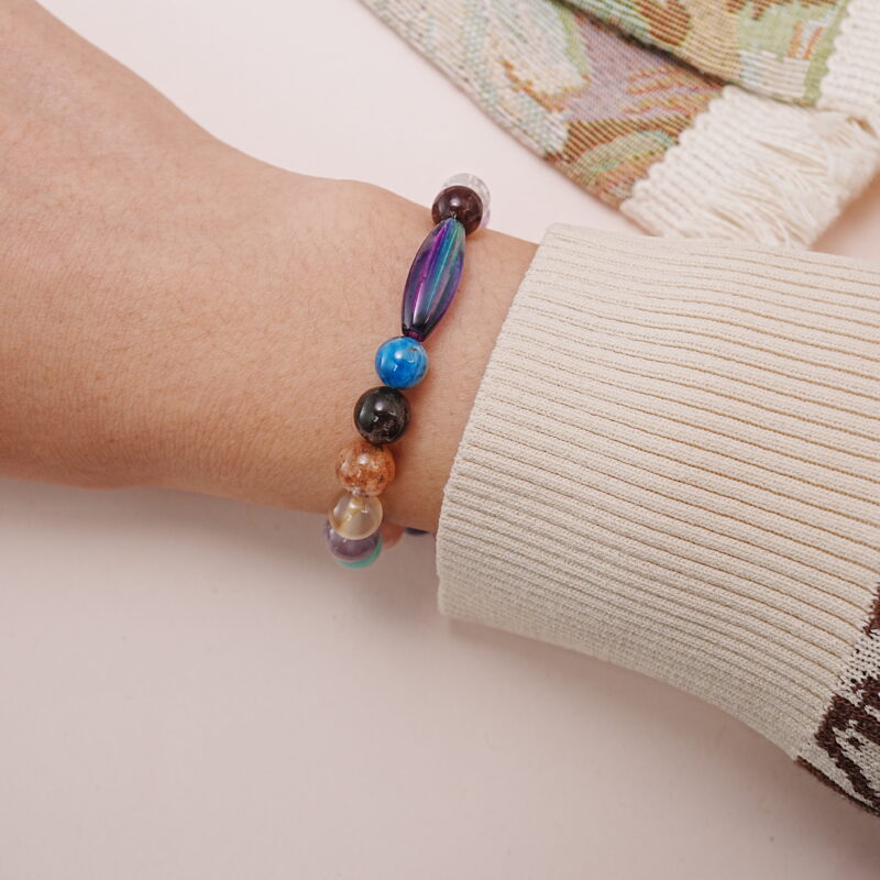 Wrist shot of a colorful multi-gemstone bracelet showing the elongated iridescent bead and mixed natural stones.