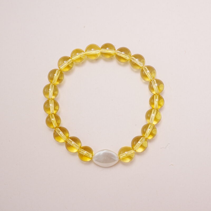 Yellow glass bead bracelet with a white oval accent charm displayed on a soft pink background.