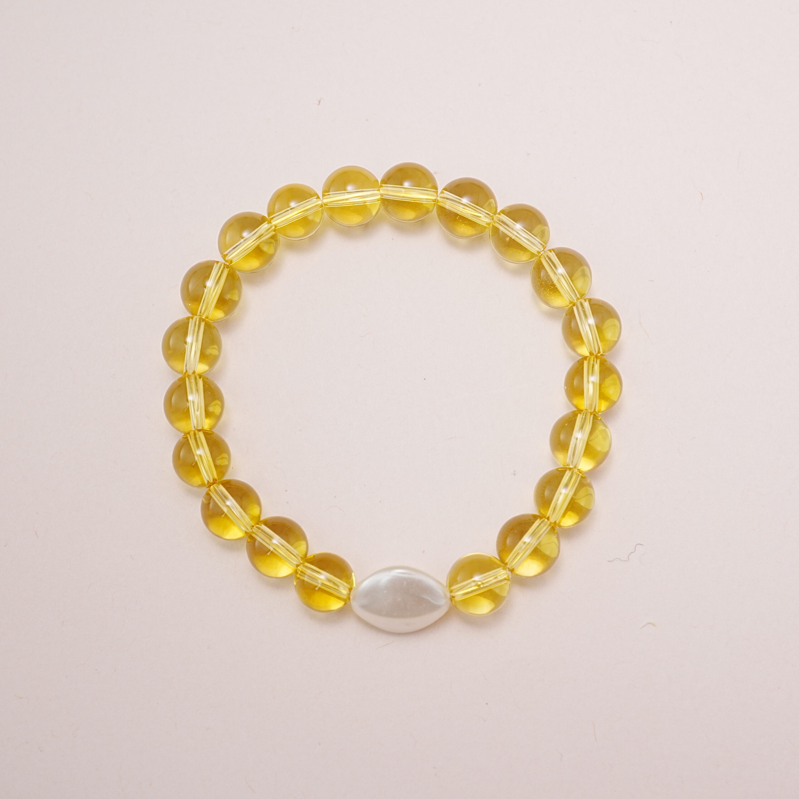yellow-glass-bead-bracelet-with-white-oval-charm-main.jpg Yellow glass bead bracelet with a white oval accent charm displayed on a soft pink background.