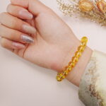 Yellow glass bead bracelet with a white oval charm shown on the inner wrist in natural lighting.