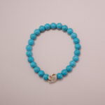 Turquoise stone bracelet with a white skull charm in the center, showcasing a simple and bold design.