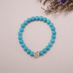 Turquoise bracelet with skull charm displayed in a minimalist scene, showcasing its vibrant color and unique design.