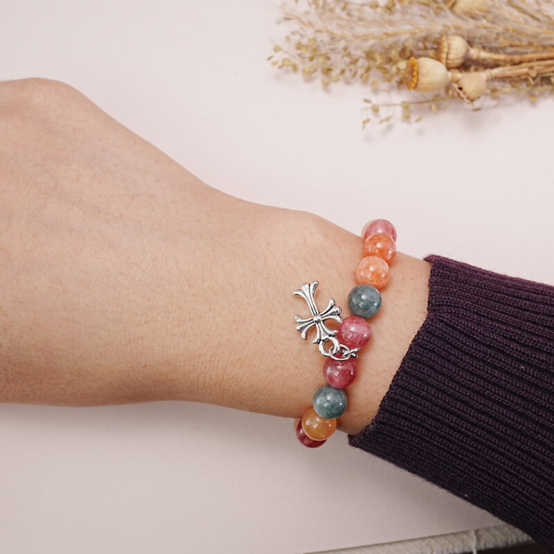 Colorful chalcedony bracelet with a silver heart charm worn on a wrist, displayed with a soft background.