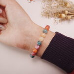 Colorful chalcedony bracelet with a silver heart charm worn on a wrist, displayed with a soft background.