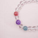 Close-up of clear quartz beads with red, purple, and teal gemstone accents