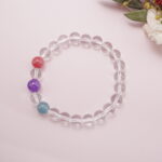 Clear quartz bracelet arranged in a flat lay with three colorful gemstone beads