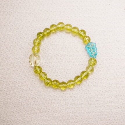 Peridot beaded bracelet with an accent carved bead displayed on a soft surface.