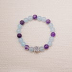 Aquamarine and amethyst beaded bracelet with a silver rose charm displayed on a soft fabric background.