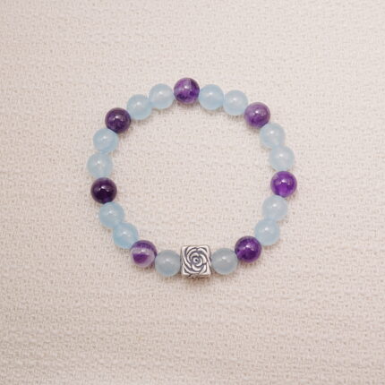 Aquamarine and amethyst beaded bracelet with a silver rose charm displayed on a soft fabric background.