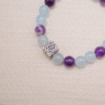 Detail view of the silver rose charm on an aquamarine and amethyst bead bracelet.