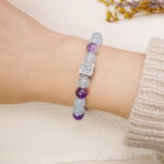 Aquamarine and amethyst bracelet with silver rose charm shown on a model’s wrist.