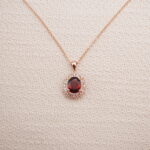 Ruby halo pendant necklace in rose gold displayed on a soft beige background.