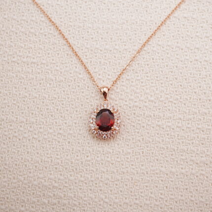 Ruby halo pendant necklace in rose gold displayed on a soft beige background.
