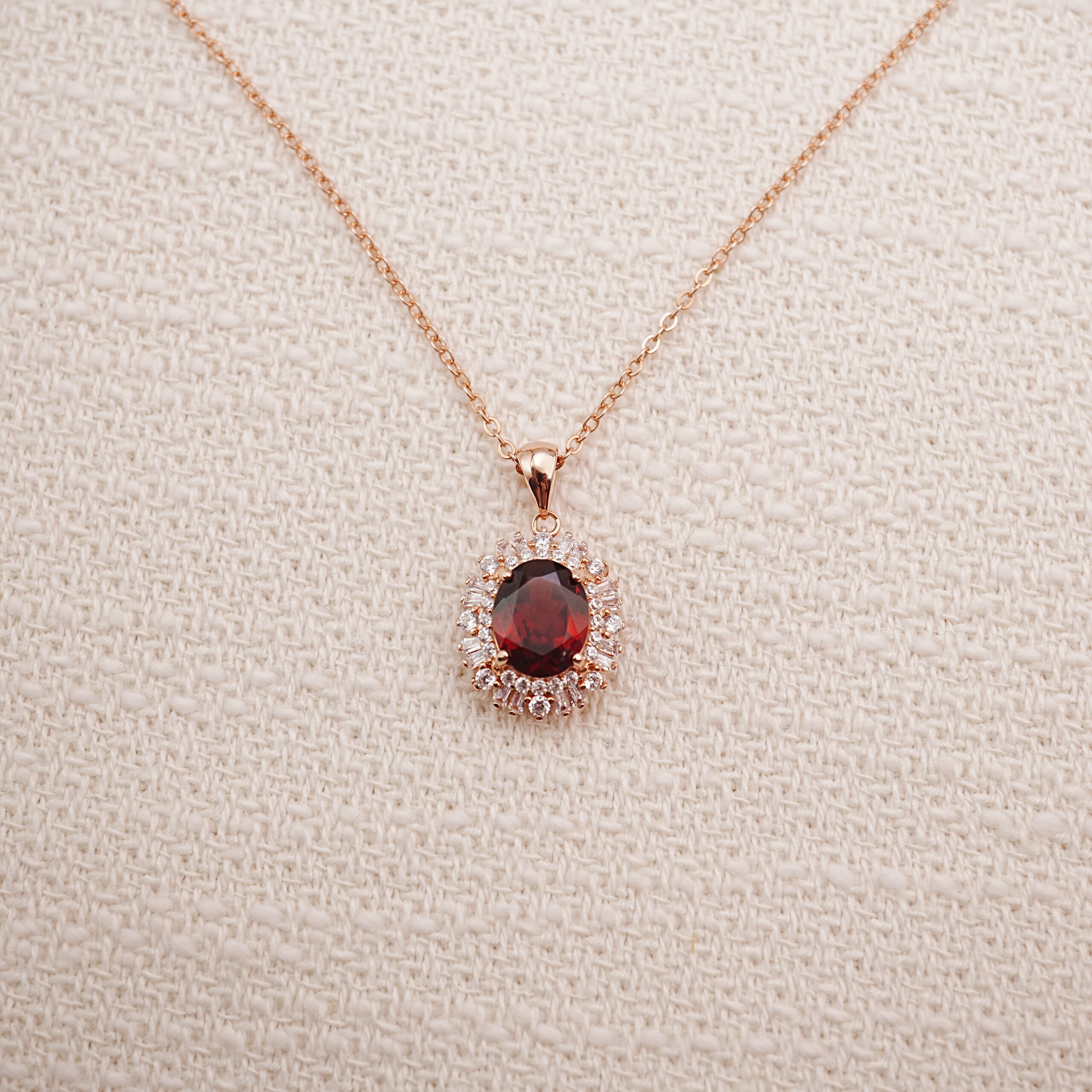 ruby-halo-pendant-necklace-main.jpg Ruby halo pendant necklace in rose gold displayed on a soft beige background.