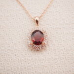 Close-up detail of the ruby halo pendant showing the vivid red gemstone and sparkling halo setting.